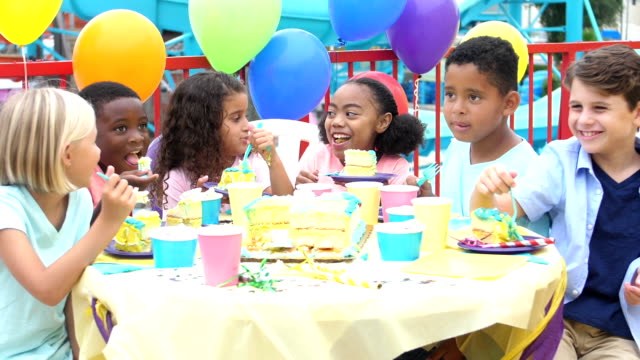 A group of six multi-ethnic children, 6 to 8 years old, having fun at a birthday party, eating cake.